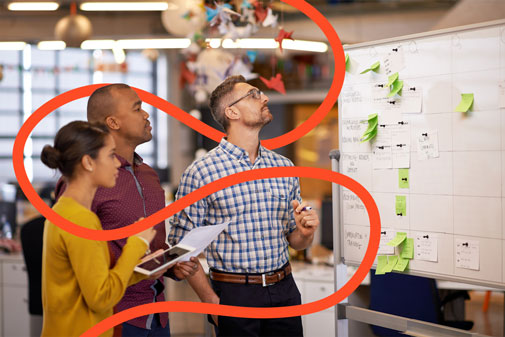 Tres companys de feina observen una pissarra amb notes adhesives en una oficina.