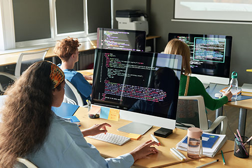 Equipo de programadores trabajando frente a monitores con código en una oficina de desarrollo tecnológico