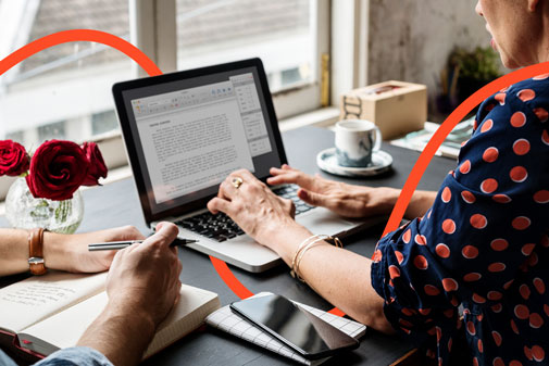 Profesional editando un documento de texto en un portátil junto a otra persona tomando notas a mano