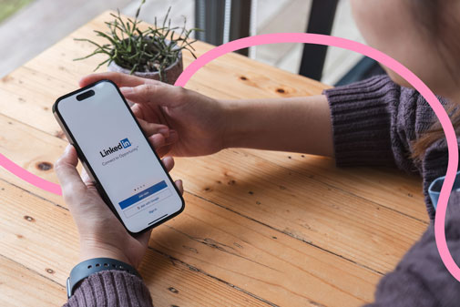 Persona sostenint un mòbil amb la pantalla d'inici de LinkedIn, sobre una taula de fusta.